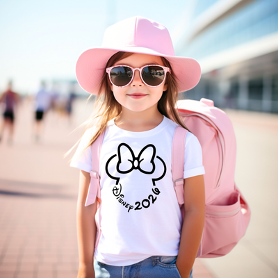 Child wearing a white t-shirt with a Disney 2026 logo, pink hat, and sunglasses, standing outdoors.
