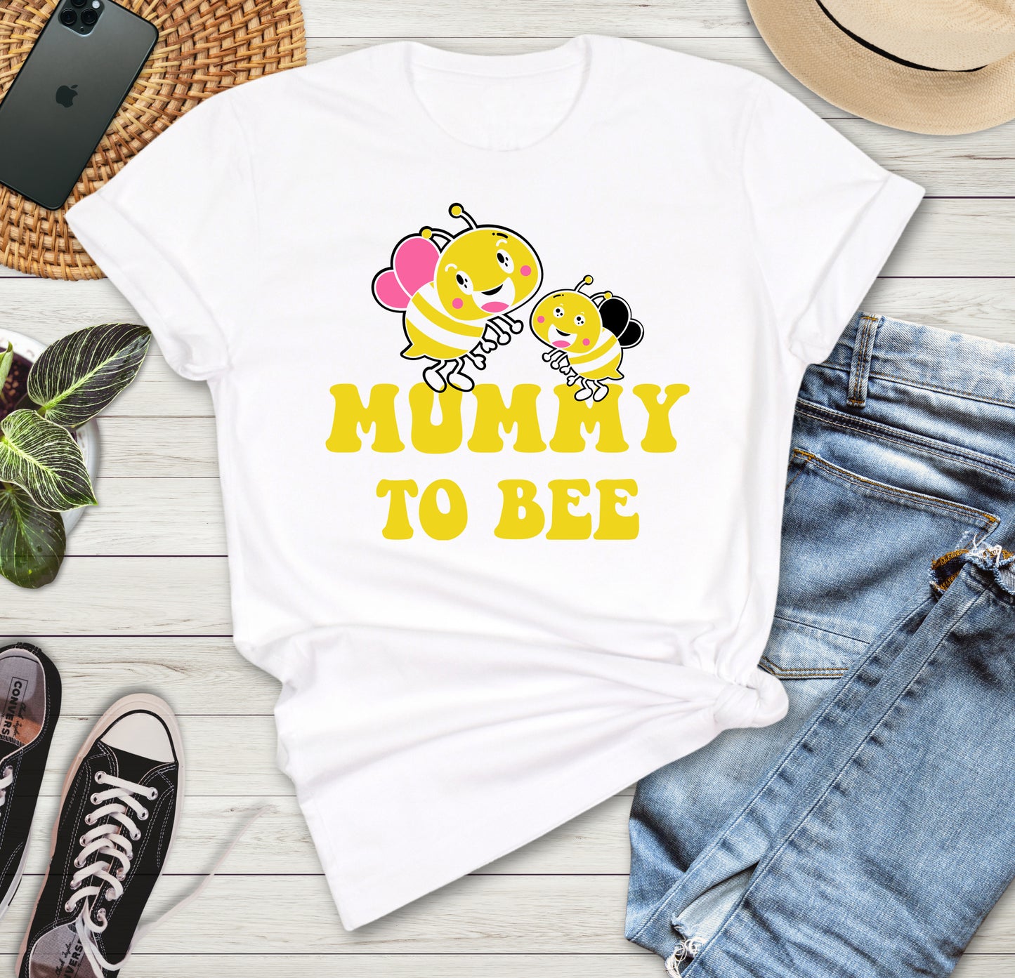 White t-shirt with 'Mummy to Bee' design on a wooden surface with jeans, sneakers, and a phone.