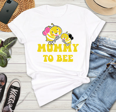 White t-shirt with 'Mummy to Bee' design on a wooden surface with jeans, sneakers, and a phone.