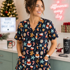 Woman wearing a festive scrub top in a medical setting with Christmas decorations.