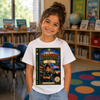 A young girl with her hair in a bun stands in a children's library wearing a white t-shirt with a large graphic print of a book titled 'Paramedic Adventure: Emergency Services'. The background shows bookshelves, a globe, and colorful floor circles.