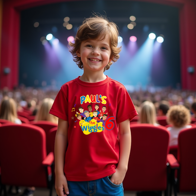 Child wearing a red 'The Wiggles' shirt in an auditorium with red seats and stage lights.