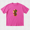 A bright pink short-sleeve crewneck t-shirt featuring a central graphic of a donut-shaped cookie decorated with chocolate frosting, colorful sprinkles, and a green candy, with a small brown bear sitting on top.