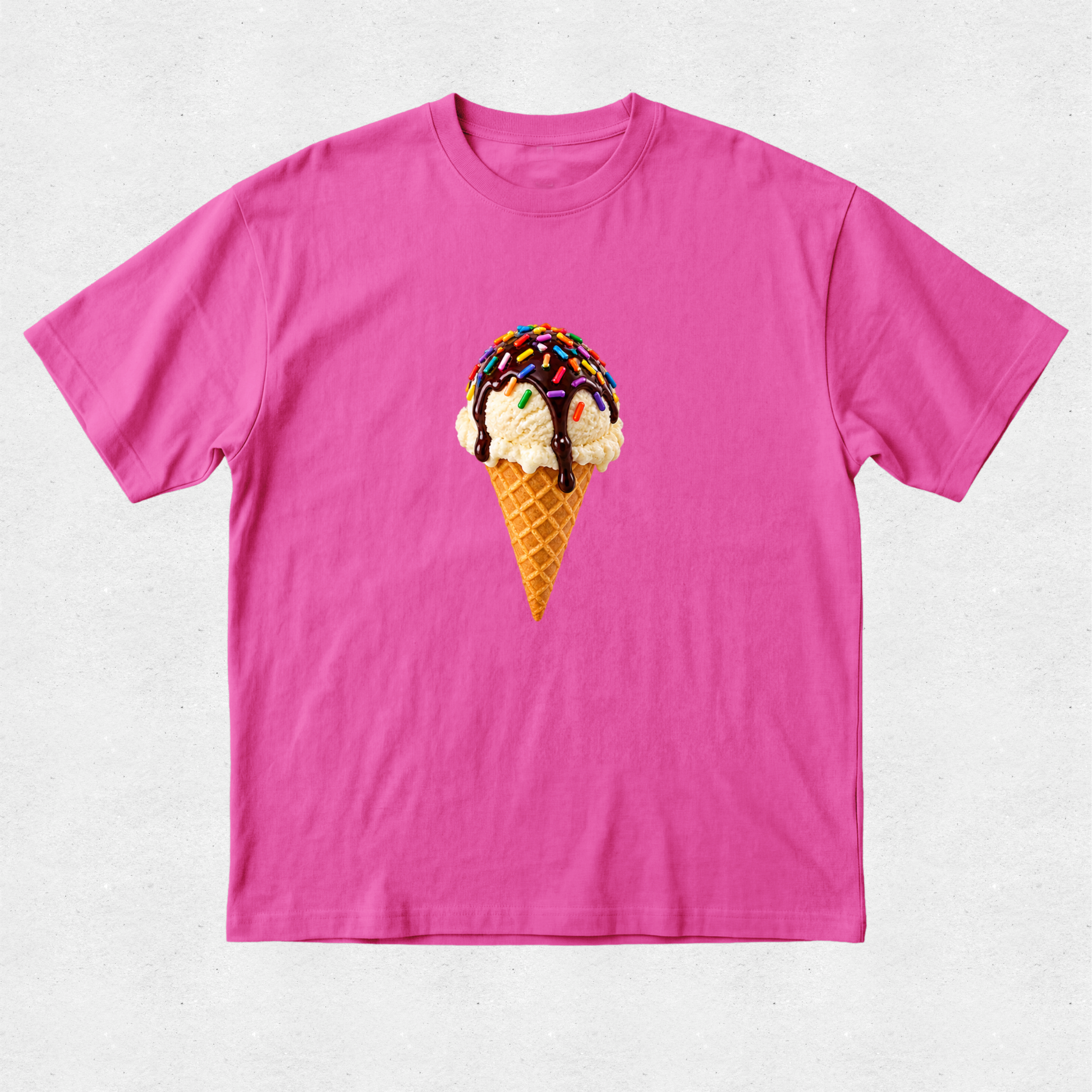 A bright pink short-sleeve crewneck t-shirt featuring a graphic of a vanilla ice cream scoop in a waffle cone with chocolate drizzle and sprinkles, displayed on a light gray textured background.