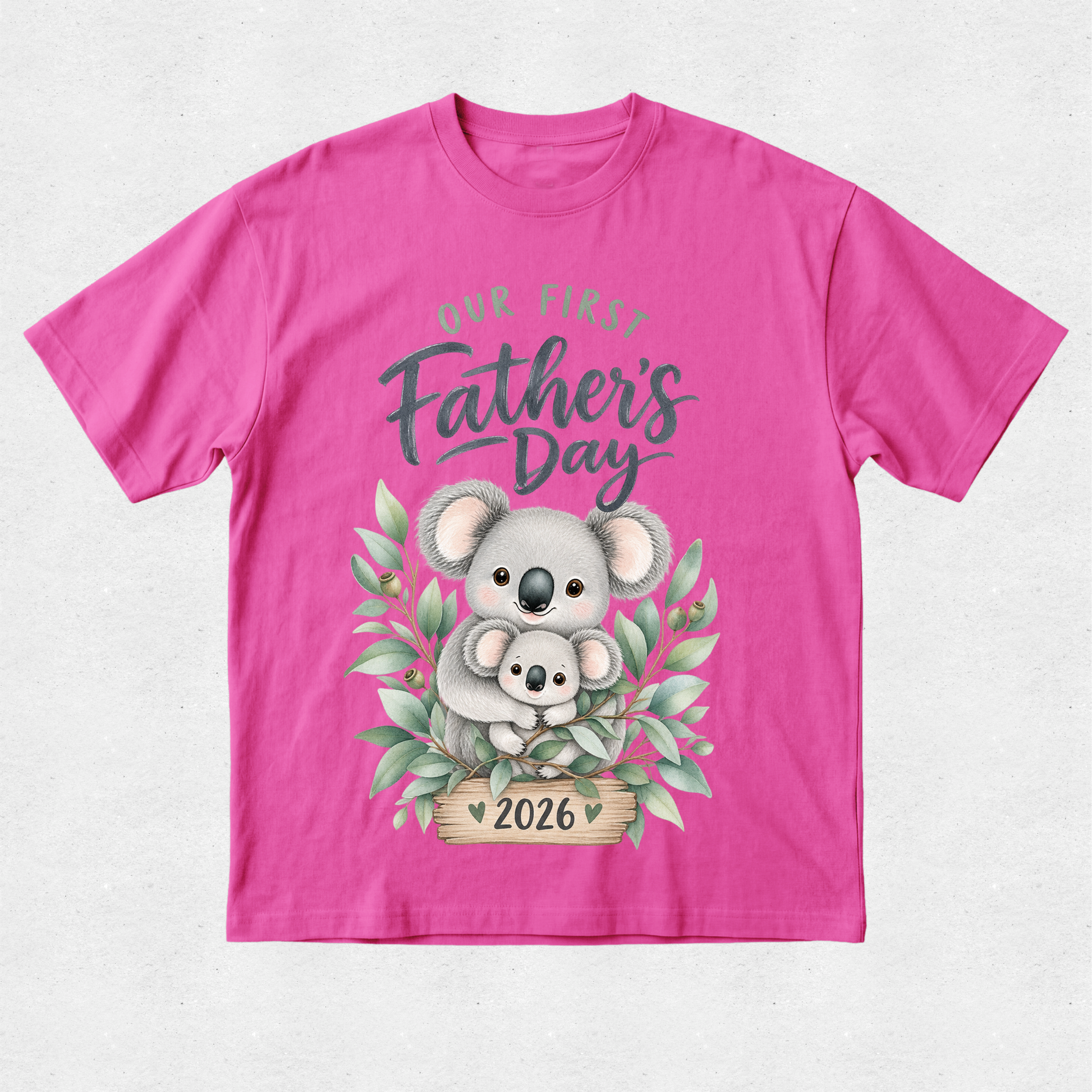 A bright pink short-sleeve t-shirt with a 'Our First Father's Day 2026' graphic featuring a cute koala illustration on a light gray textured background.