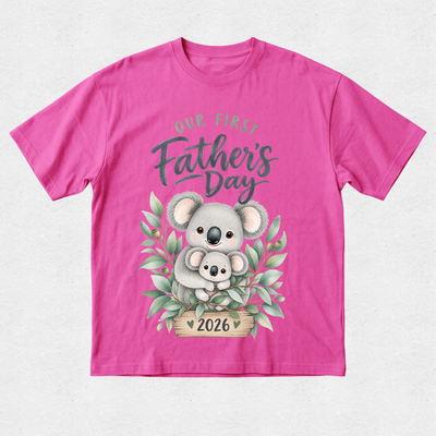 A bright pink short-sleeve t-shirt with a 'Our First Father's Day 2026' graphic featuring a cute koala illustration on a light gray textured background.
