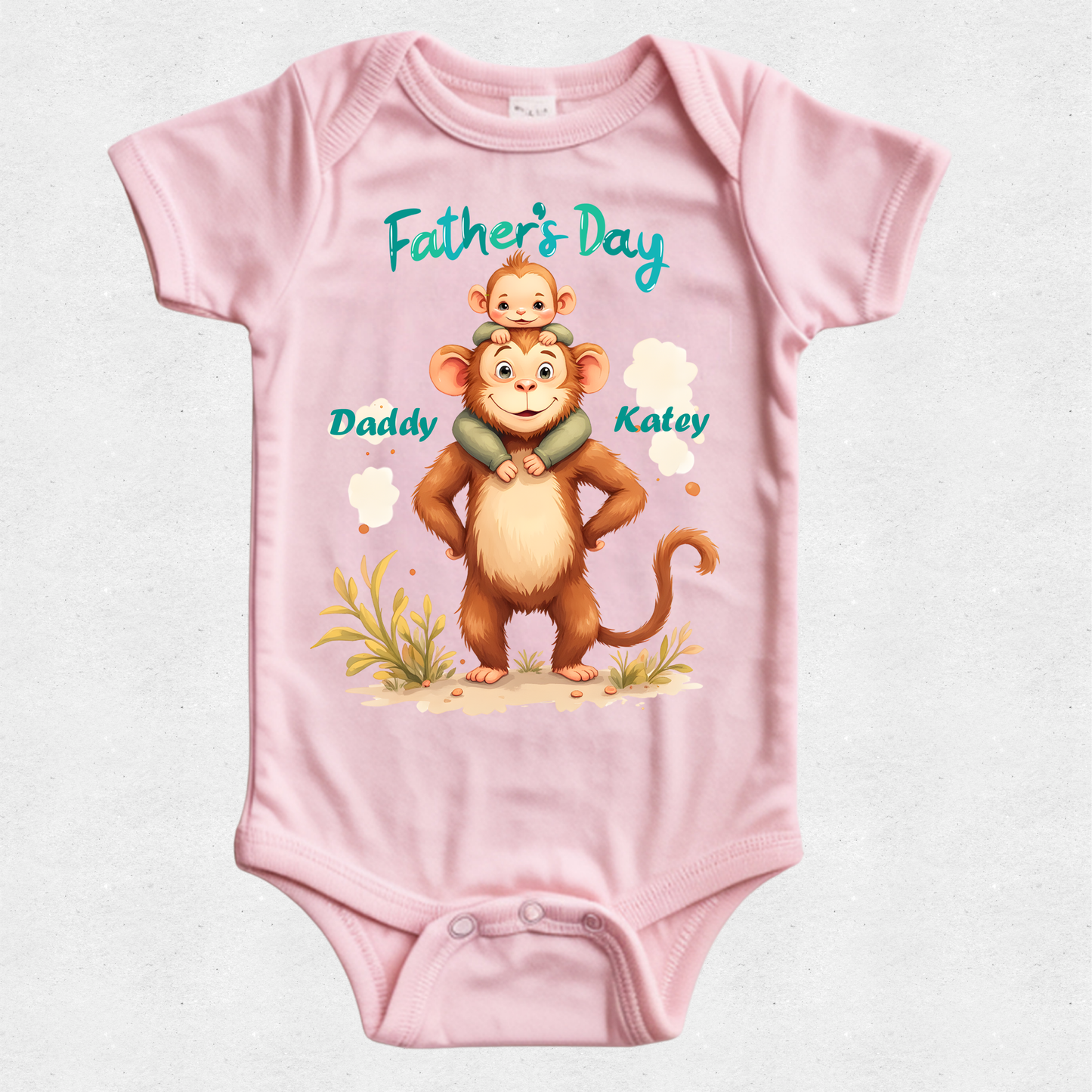 A light pink short-sleeve baby bodysuit with a custom Father's Day graphic. The graphic features an illustration of a brown monkey carrying a small baby on its back, with the text 'Father's Day' in teal, 'Daddy' next to the monkey, and 'Kaley' next to the monkey's head.