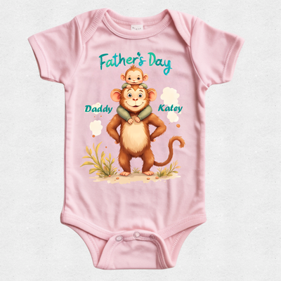 A light pink short-sleeve baby bodysuit with a custom Father's Day graphic. The graphic features an illustration of a brown monkey carrying a small baby on its back, with the text 'Father's Day' in teal, 'Daddy' next to the monkey, and 'Kaley' next to the monkey's head.