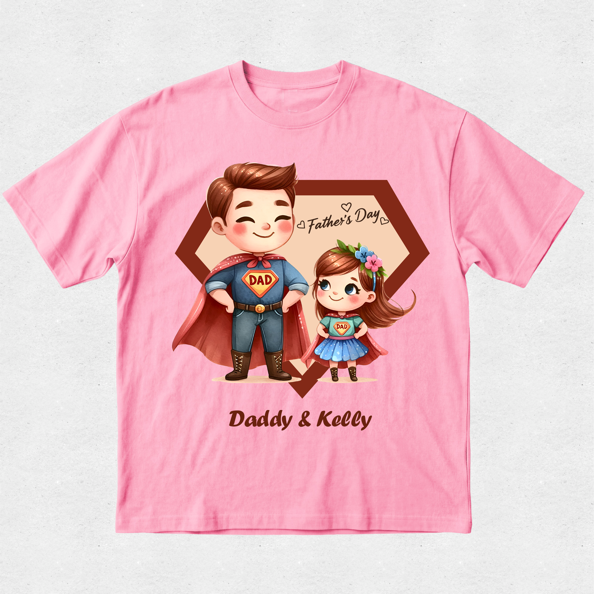 A pink short-sleeve crewneck t-shirt featuring a custom cartoon graphic of a father and daughter in superhero costumes, with 'Father's Day' and 'Daddy & Kelly' printed on the front.