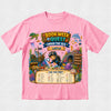 A pink short-sleeve crewneck t-shirt featuring a colorful cartoon graphic of an underwater book-themed adventure titled 'Book Week Quest Under the Sea Layla'. The graphic includes illustrations of a diver, sea creatures, a treasure chest, and a 'Can You Find?' checklist at the bottom, displayed on a light gray textured background.