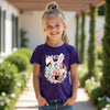 Young girl wearing a purple t-shirt with a colorful graphic design outdoors.