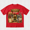 A red short-sleeve crewneck t-shirt featuring a large, colorful graphic print on the front. The graphic is themed around a children's book series titled 'Book Week Quest: Rescue Heroes' and depicts an illustration of a young boy in a firefighter helmet, a Dalmatian, ambulances, a fire station, and a doghouse.