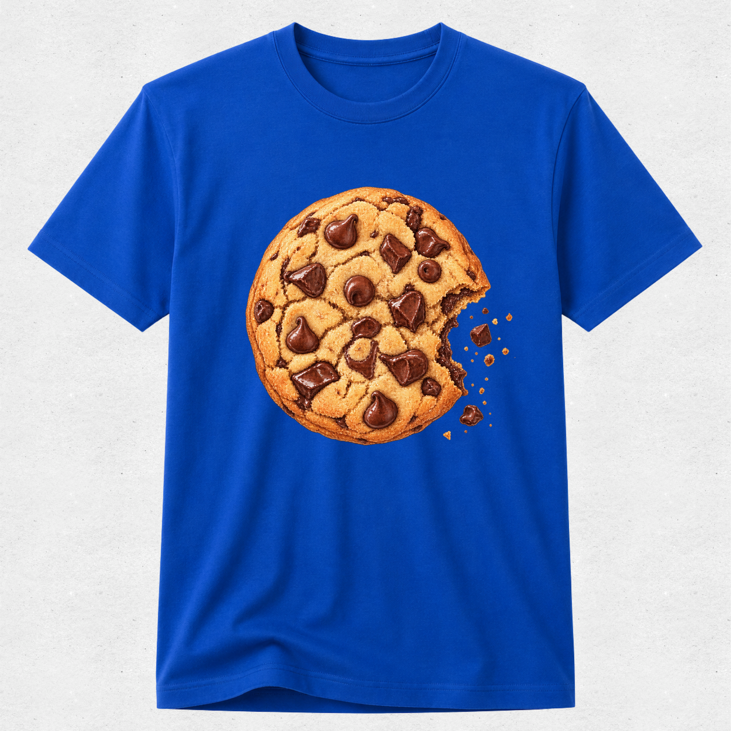 A royal blue short-sleeve crewneck t-shirt featuring a large graphic print of a chocolate chip cookie with a bite taken out, displayed on a light gray textured background.