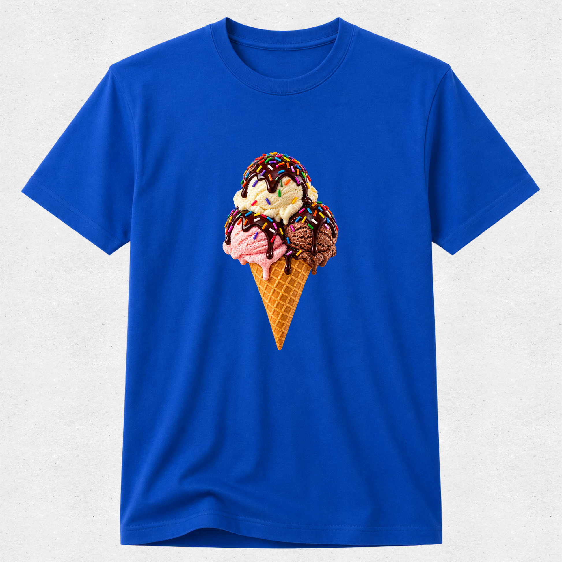 A royal blue short-sleeve crewneck t-shirt featuring a graphic print of a waffle cone filled with three ice cream scoops (pink, vanilla, and chocolate) topped with chocolate drizzle, displayed on a light gray textured background.