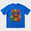 A bright blue short-sleeve t-shirt with a colorful graphic on the front that reads 'RAD LIKE DAD' with a cartoon emoji wearing sunglasses and a cap, set against a light gray textured background.