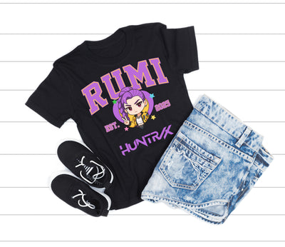 Black t-shirt with 'RUMI' and 'HUNTRIX' text, socks, and denim shorts on a white wooden surface