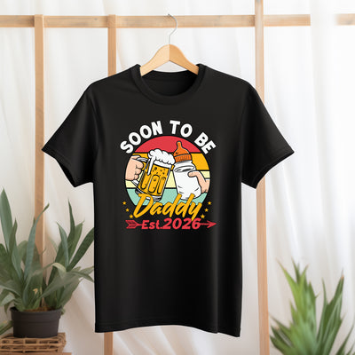 Black t-shirt with 'Soon to be Daddy Est. 2026' graphic design on a hanger against a light background.