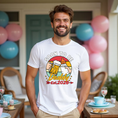 Man wearing a 'Soon to be Daddy Est. 2026' t-shirt with balloons in the background.