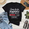 Black t-shirt with 'Soon to be Mummy 2026 Loading' text on a wooden surface with jeans, sneakers, and a phone.