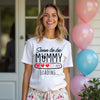 Woman wearing a white t-shirt with 'Soon to be Mummy Loading 2026' text, standing in front of balloons.