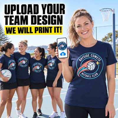 A woman on an outdoor basketball court wears a navy blue custom team t-shirt with a circular 'Bayside Comes My Netball Club' logo. She holds up a smartphone showing a matching digital design template.