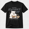 A black short-sleeve crewneck t-shirt featuring a custom Father's Day graphic of a white polar bear and a small cub reading a book, with the text 'OUR FIRST FATHER'S DAY', 'DADDY + PATRICK', and '2026' on a light gray background.