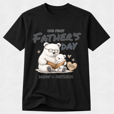 A black short-sleeve crewneck t-shirt featuring a custom Father's Day graphic of a white polar bear and a small cub reading a book, with the text 'OUR FIRST FATHER'S DAY', 'DADDY + PATRICK', and '2026' on a light gray background.
