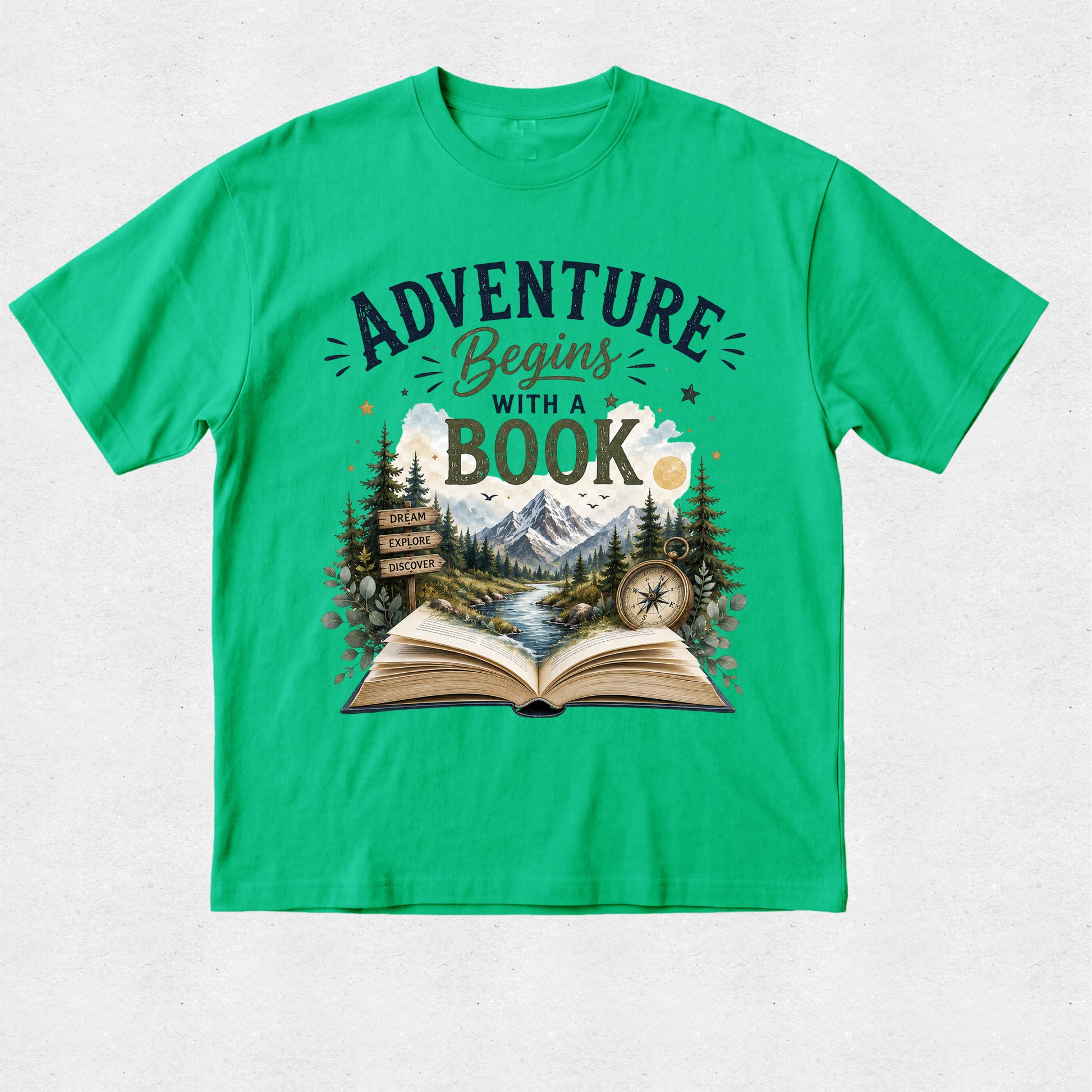 A bright green short-sleeve crewneck t-shirt with a detailed graphic on the front. The graphic features the text 'ADVENTURE Begins WITH A BOOK' in dark green and brown lettering above an illustration of an open book, mountains, pine trees, a river, and a compass.