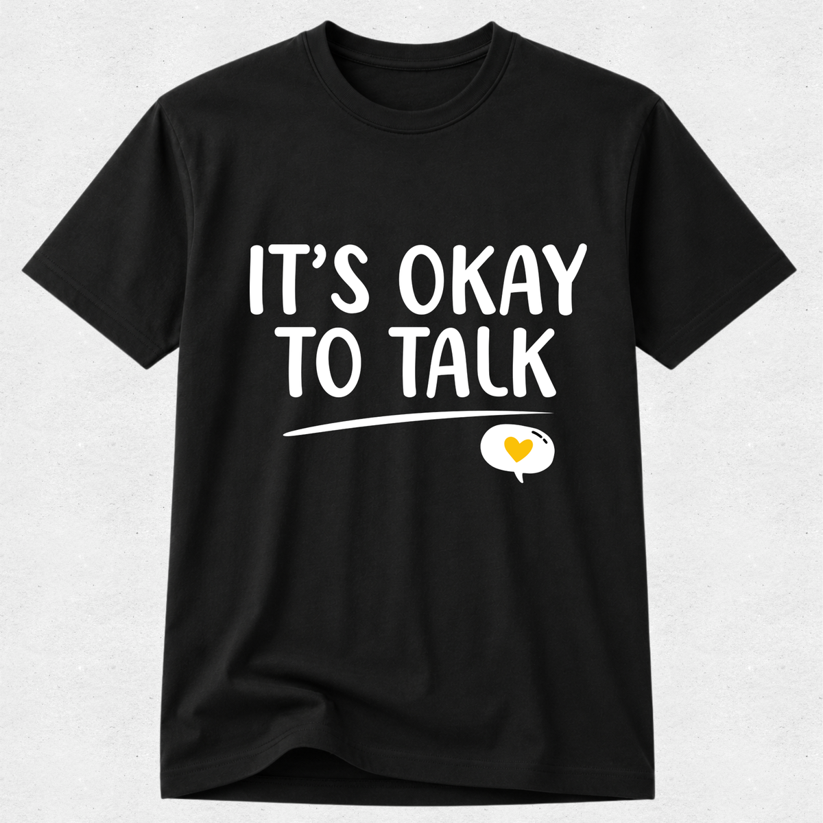 A black short-sleeve crewneck t-shirt with the text 'IT'S OKAY TO TALK' printed in white across the chest, underlined, with a speech bubble containing a small yellow heart below.