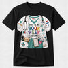 A black short-sleeve crewneck t-shirt featuring a colorful graphic print of a bookish doctor costume. The graphic depicts a white and teal scrub top with a stethoscope, medical badges, a teddy bear in a pocket, and the text 'THIS IS MY BOOK WEEK COSTUME!' in multicolored letters.