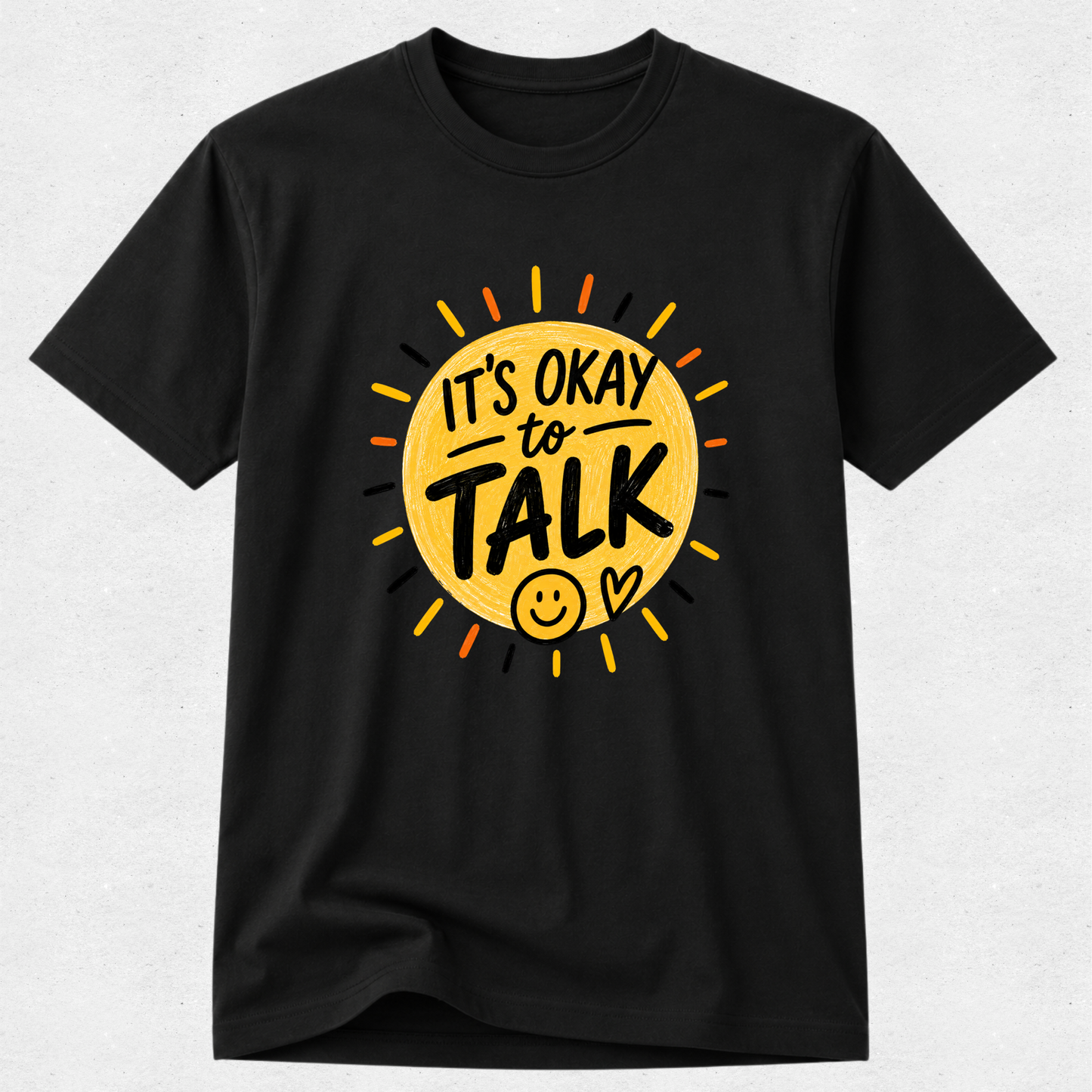 A black short-sleeve crewneck t-shirt featuring a graphic print of a yellow sun with the text 'IT'S OKAY to TALK' in black, along with a smiley face and heart, displayed on a light gray textured background.