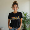 Woman wearing a black t-shirt with 'NAIDOC Week 50 Years Deadly' text, standing indoors with a plant in the background.