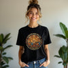 Woman wearing a black t-shirt with a design and text, standing indoors with plants in the background.