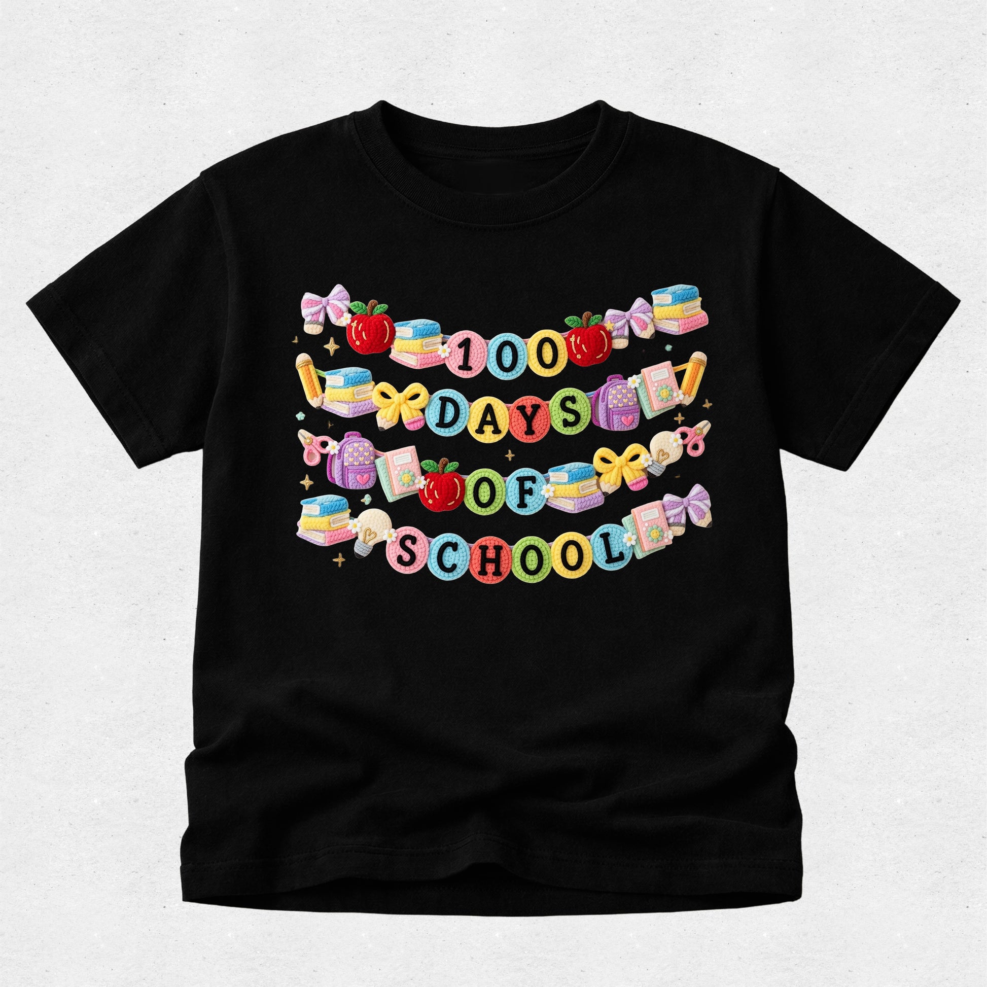 A black short-sleeve t-shirt with a colorful graphic that reads '100 DAYS TO SCHOOL' decorated with school-themed illustrations like apples, books, and bows, shown on a light gray background.