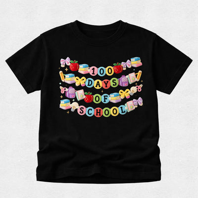 A black short-sleeve t-shirt with a colorful graphic that reads '100 DAYS TO SCHOOL' decorated with school-themed illustrations like apples, books, and bows, shown on a light gray background.