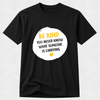 A black short-sleeve crewneck t-shirt with a white circular graphic on the chest containing the text 'BE KIND YOU NEVER KNOW WHAT SOMEONE IS CARRYING' in yellow and black, with a small yellow heart at the bottom.