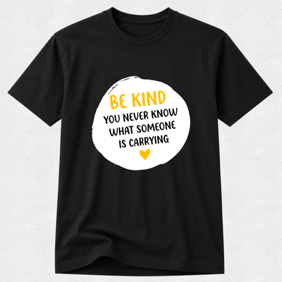 A black short-sleeve crewneck t-shirt with a white circular graphic on the chest containing the text 'BE KIND YOU NEVER KNOW WHAT SOMEONE IS CARRYING' in yellow and black, with a small yellow heart at the bottom.