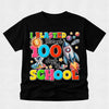 A black short-sleeve t-shirt with a colorful retro graphic celebrating '100 days of SCHOOL' with space-themed illustrations like a rocket, astronaut, and sun, displayed on a light gray textured background.