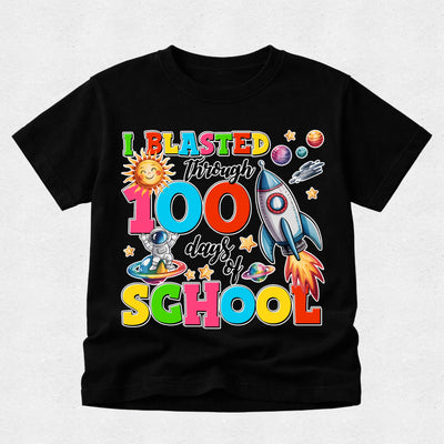 A black short-sleeve t-shirt with a colorful retro graphic celebrating '100 days of SCHOOL' with space-themed illustrations like a rocket, astronaut, and sun, displayed on a light gray textured background.