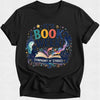 A black short-sleeve crewneck t-shirt with a colorful graphic on the front that reads 'IT'S BOOK WEEK! SYMPHONY OF STORIES' with an illustration of an open book, stars, and magical elements.