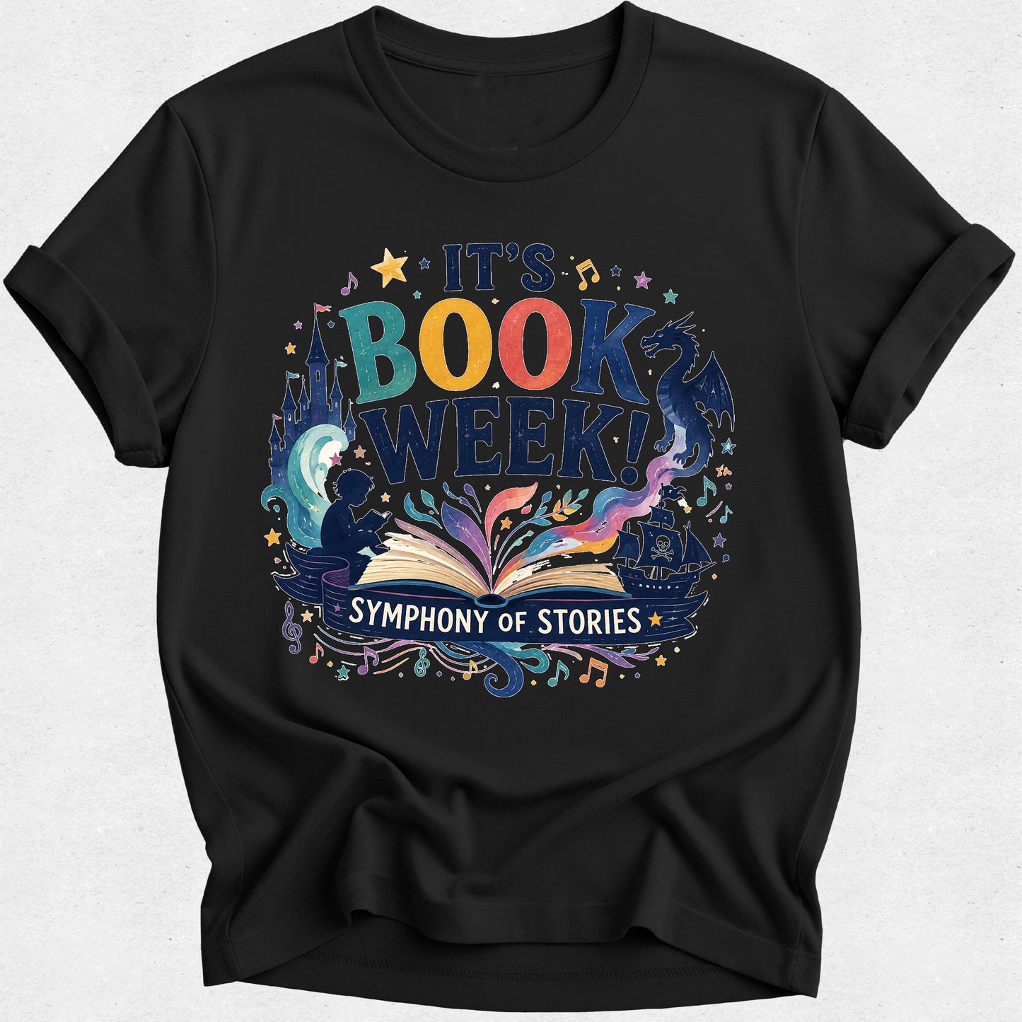 A black short-sleeve crewneck t-shirt with a colorful graphic on the front that reads 'IT'S BOOK WEEK! SYMPHONY OF STORIES' with an illustration of an open book, stars, and magical elements.
