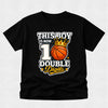 A black short-sleeve t-shirt with a graphic print that reads 'THIS BOY IS NOW 1 DOUBLE Digits' around an orange basketball with a gold crown, displayed on a light gray textured background.