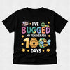 A black short-sleeve t-shirt with a colorful graphic design celebrating a teacher's 100th day, featuring cartoon bees, a beehive, stars, and the text 'I'VE BUGGED MY TEACHER FOR 100 DAYS'.