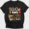 A black short-sleeve crewneck t-shirt with a graphic print that reads '100 DAYS of Coffee & Chaos' in white, leopard print, gold, and pink, accompanied by illustrations of a coffee cup, a book, and a pencil.