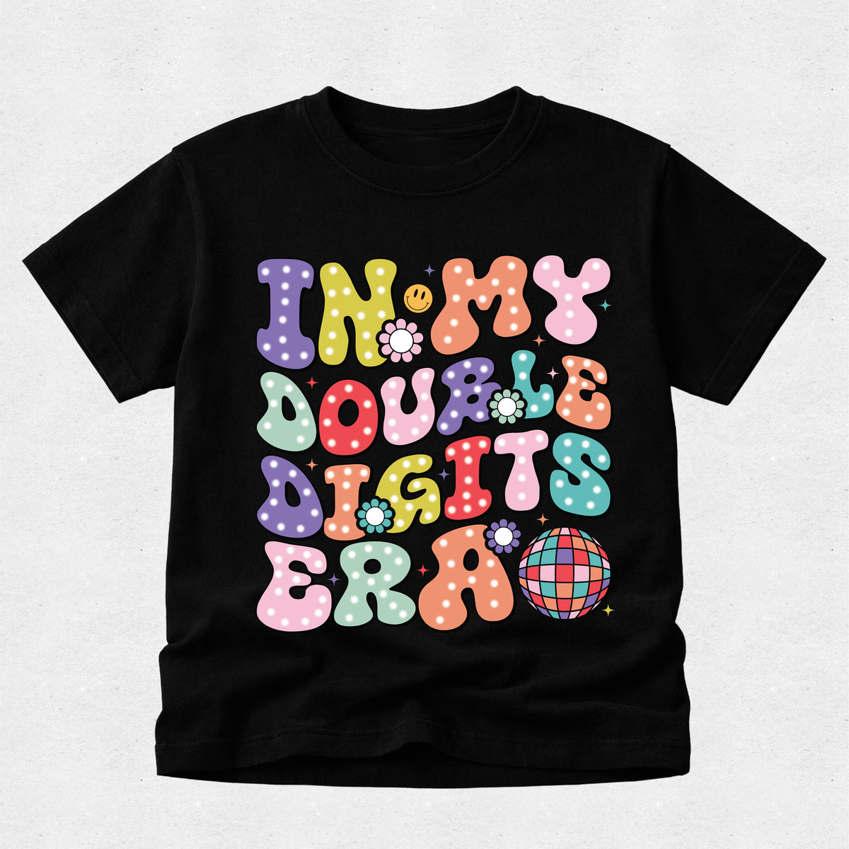 A black short-sleeve t-shirt with a colorful retro graphic that reads 'IN MY DOUBLE DIGITS ERA' in wavy, polka-dotted bubble letters, displayed on a light gray textured background.