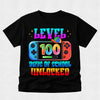 A black short-sleeve t-shirt with a colorful graphic on the front. The graphic features the text 'LEVEL 100 DAYS OF SCHOOL UNLOCKED' in a rainbow gradient font, with a Nintendo Switch console illustration in the center.