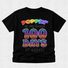 A black short-sleeve t-shirt with a colorful graphic that reads 'POPPIN' my way through 100 DAYS of school' in rainbow pop-art lettering, displayed on a light gray background.