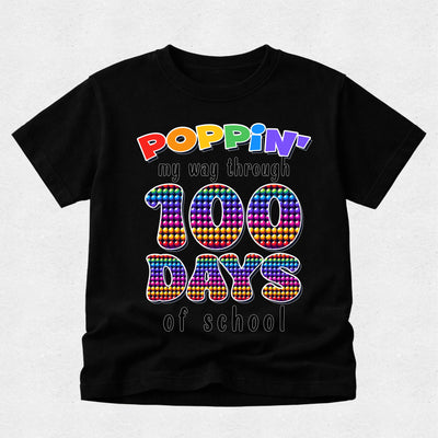 A black short-sleeve t-shirt with a colorful graphic that reads 'POPPIN' my way through 100 DAYS of school' in rainbow pop-art lettering, displayed on a light gray background.