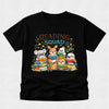 A black short-sleeve t-shirt with a colorful cartoon graphic of five cute animals reading books, with the text 'READING SQUAD' above them, displayed on a light gray background.