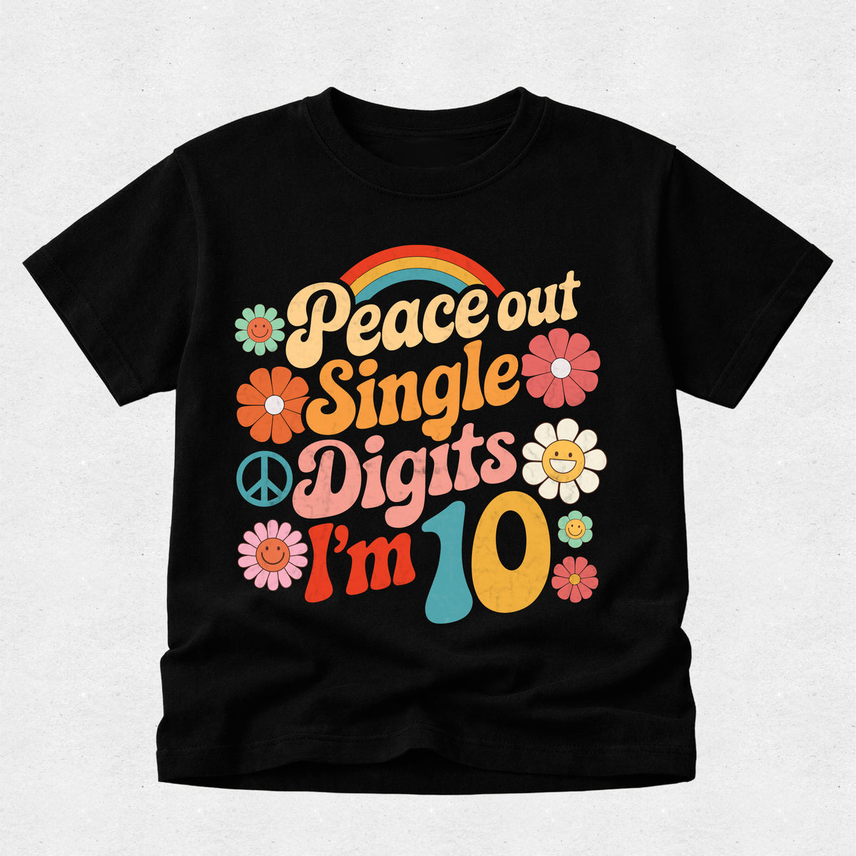 A black short-sleeve t-shirt with a retro 1960s-style graphic that reads 'Peace out Single Digits I'm 10' in colorful retro lettering, accompanied by flowers, a peace sign, and a rainbow, shown on a light gray textured background.